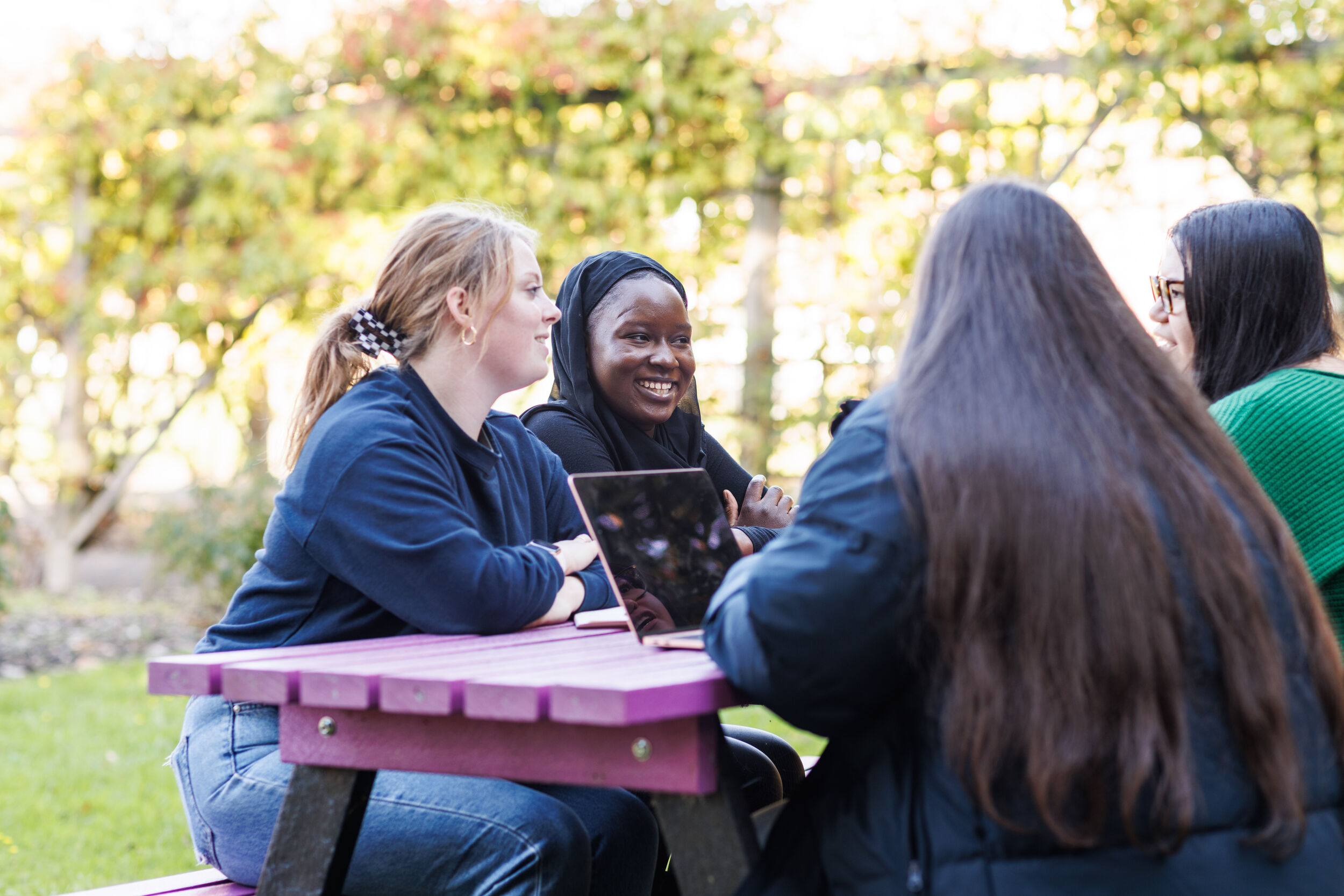 Students sit outside on a bench studying.